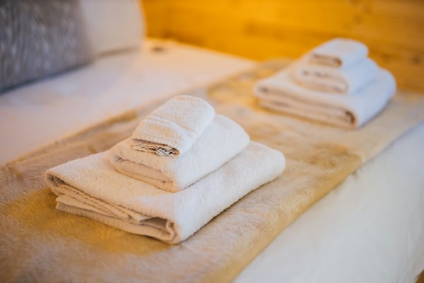 Neatly folded fresh white towels on a warm wood bed in a vacation rental