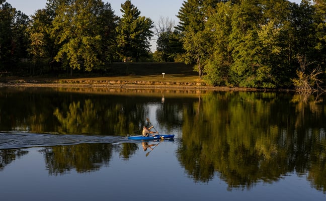 Kayaker on a calm lake with tree reflections at golden hour