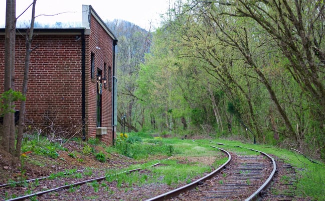 Historic brick building beside curving railroad tracks in a wooded North Carolina valley